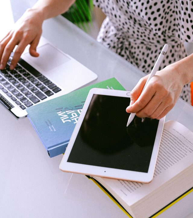 Woman multitasking with a laptop and tablet at a home office, showcasing remote work efficiency.